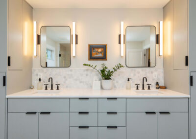 Modern bathroom with sleek grey Bulthaup style cabinets, two rectangular mirrors above double sinks, vertical light fixtures beside each mirror with hexagonal tile backsplash.